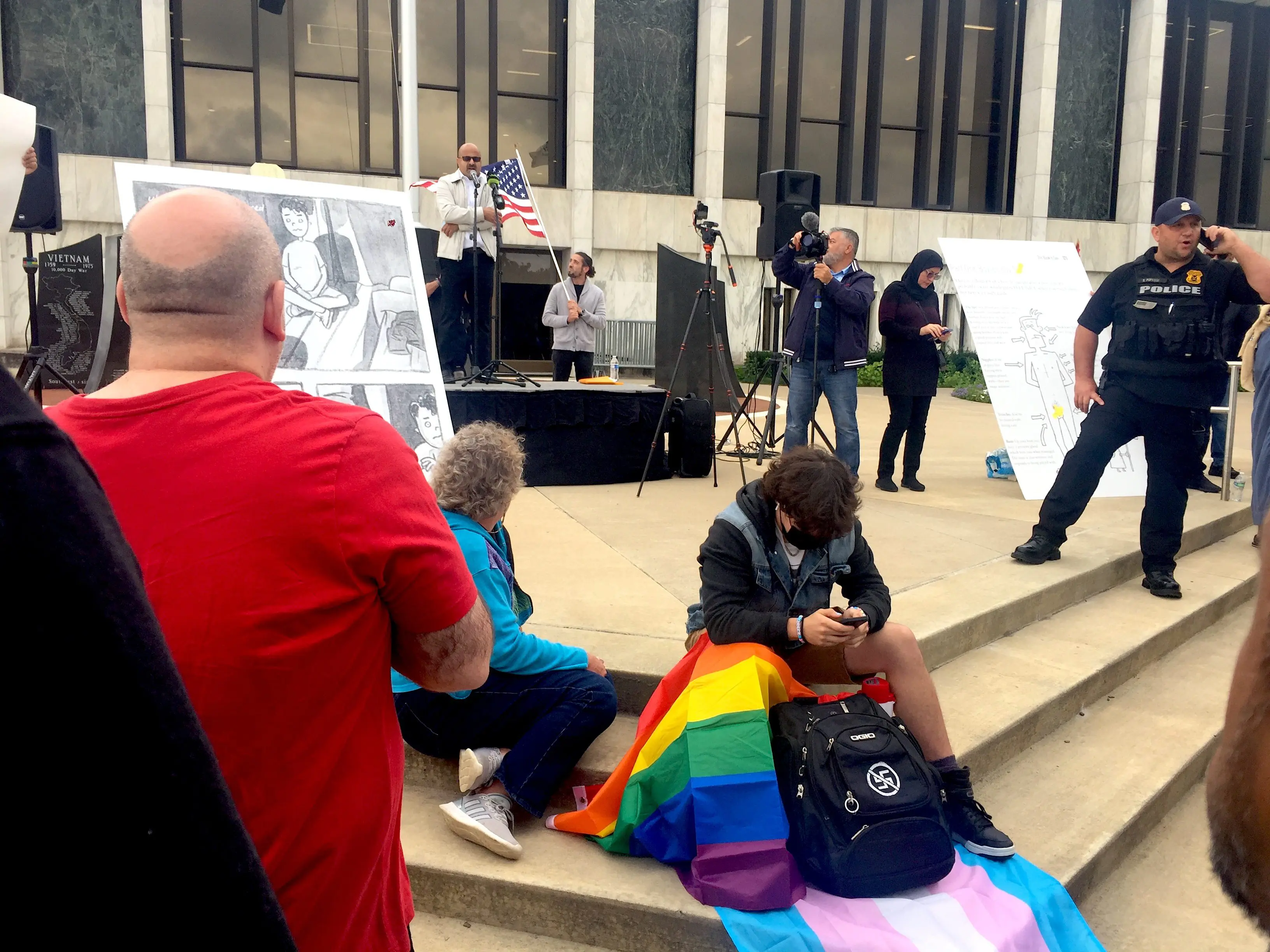 Sam Smalley sits on the steps in front of the Henry Ford Centennial Library with a pride flag to counter an ongoing protest against certain books in the Dearborn Public Schools library system. Photo: The Arab American News
