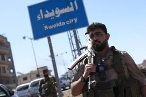 A member of Syria's security forces stands under a sign in the predominantly Druze city of Sweida, following clashes between Bedouin tribes and Druze fighters on July 15. – AFP