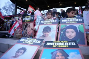 Local children carry photos of Lebanese children and families murdered by the Israeli army during the candle light vigil held at the Peace Park in wet Dearborn on Friday evening, April 10. – Photos by Abbas Shehab