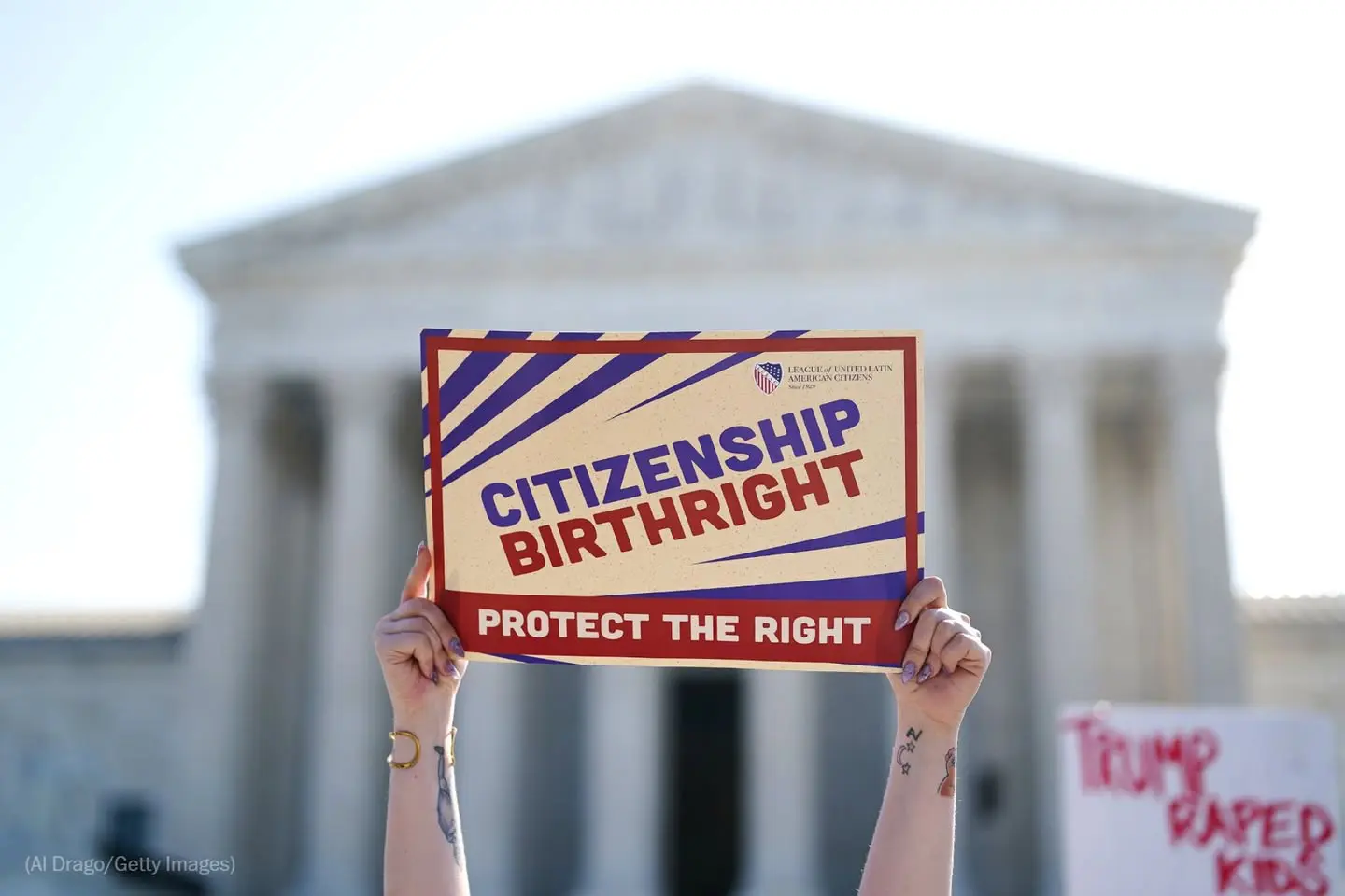 A demonstartor holds a sign infront of the U.S. Supreme Court while the Justices considering birthright citizenship – Video grab