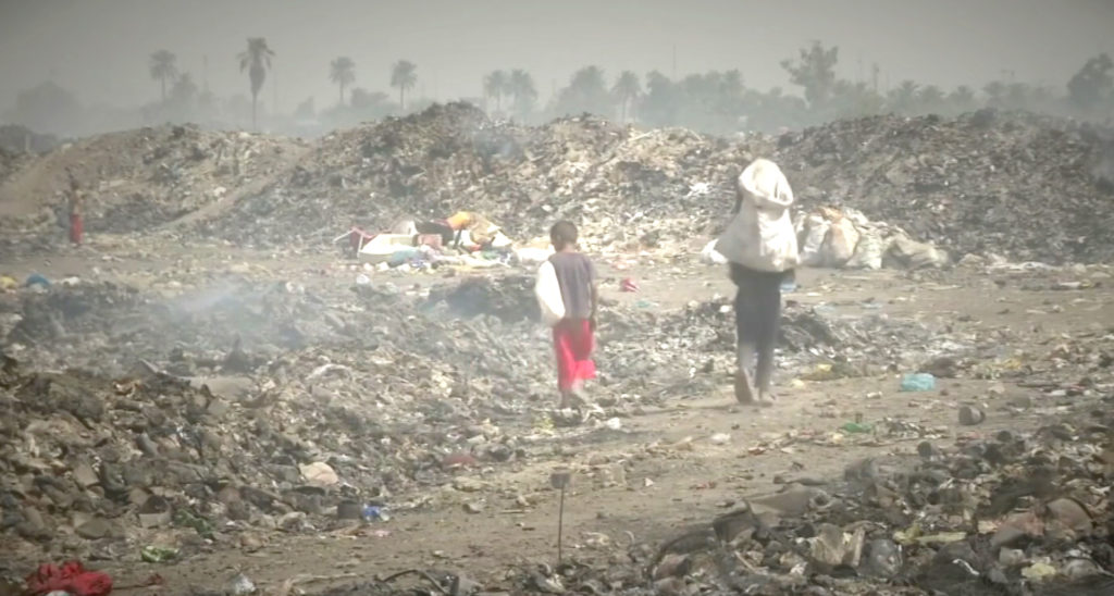 Two Iraqis walking next to piles of garbage in southern Iraq