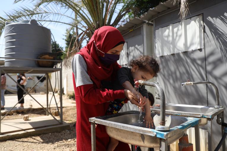 Mother Kanouz holding her one-year old daughter Fatima to wash her hands at Mhamara informal settlement, July 5. Photo: UNICEF