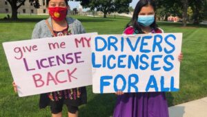 Maria Hernandez-Torres, left, poses with a sign that reads "give me my license back" at a protest in Lansing, Mich. on Sept. 16, 2020. (WWMT/Genevieve Grippo)