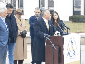 Attorney Nabih Ayad, founder of the Arab American Civil Rights League, speaks at the press conference. Behind him, from left, are Osama Siblani, publisher of The Arab American News; Nasser Baydoun; Abed Ayoub, national executive director of the ADC; ACRL President Jim Allen and ACRL Executive Director Mariam Charara.– Photo courtesy of Michigan Radio