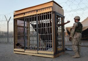 A detainee in an outdoor solitary confinement cell talks with a military officer at the Abu Ghraib Prison in June 2004.