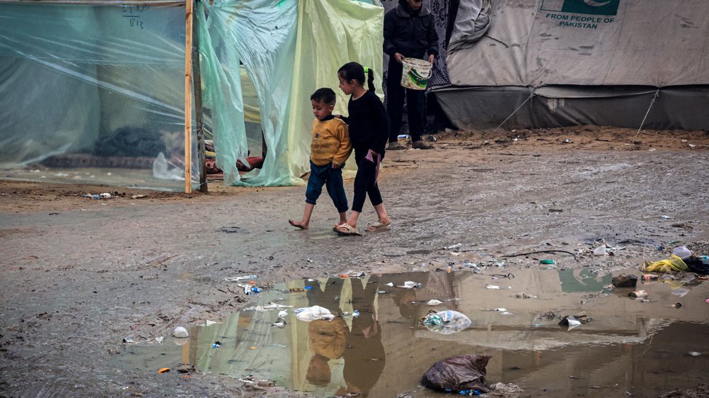 Palestinian children walk on a muddy path past tents at a makeshift camp housing displaced Palestinians, in Rafah in the southern Gaza Strip, amid the ongoing conflict between Israel and Hamas, on January 2, 2024.