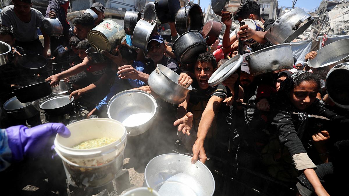 Palestinians wait to receive food cooked by a charity kitchen, in Beit Lahia, northern Gaza Strip, May 8, 2025. | Photo Credit: Reuters